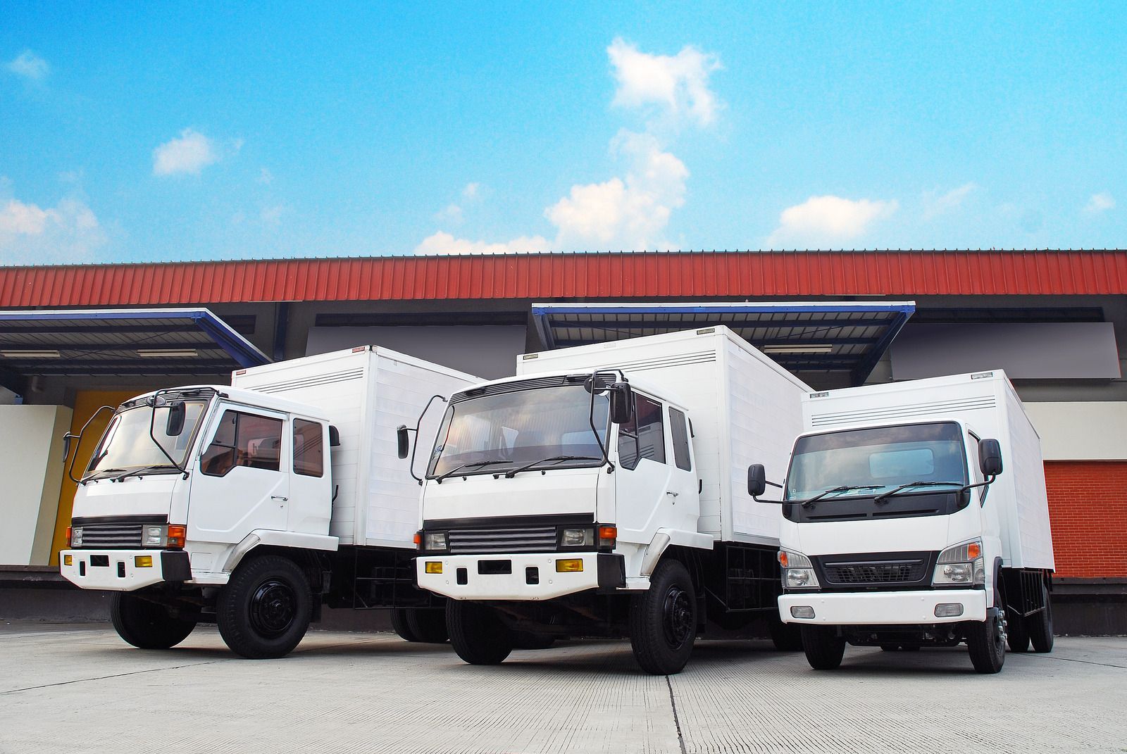 Three white delivery trucks parked outside a warehouse under a blue sky.