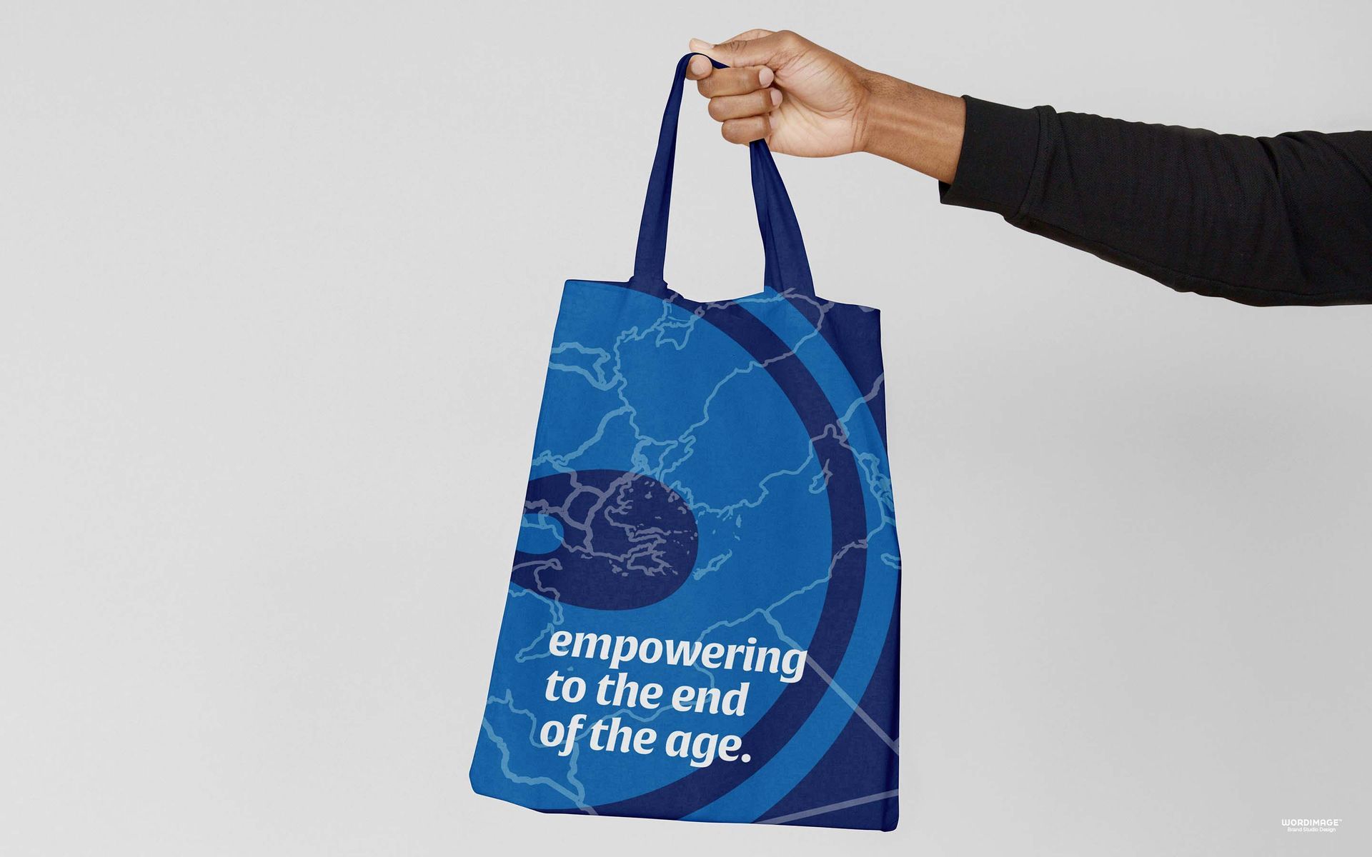 A person is holding a blue tote bag that says empowering to the end of the age