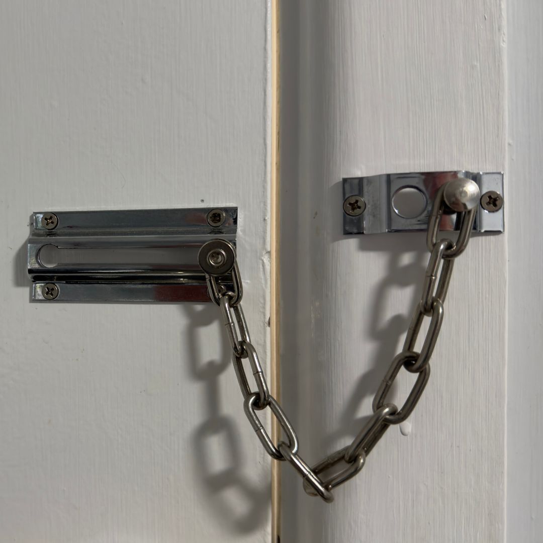 Een zilveren kettingslot beveiligt een witte deur met een slot in het kozijn.