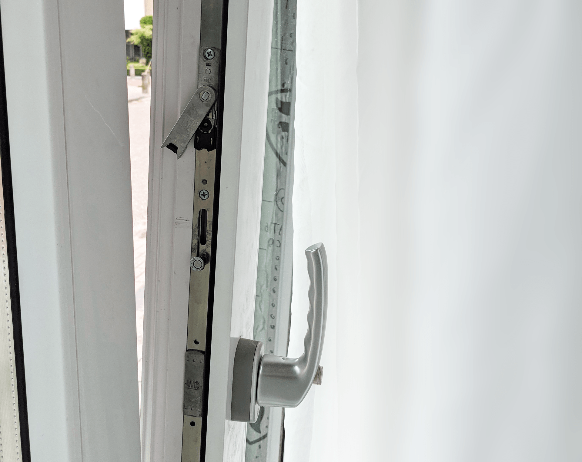 Detailopname van een wit deurkozijn met een zilverkleurige handgreep en een gedeeltelijk openstaande sluiting.