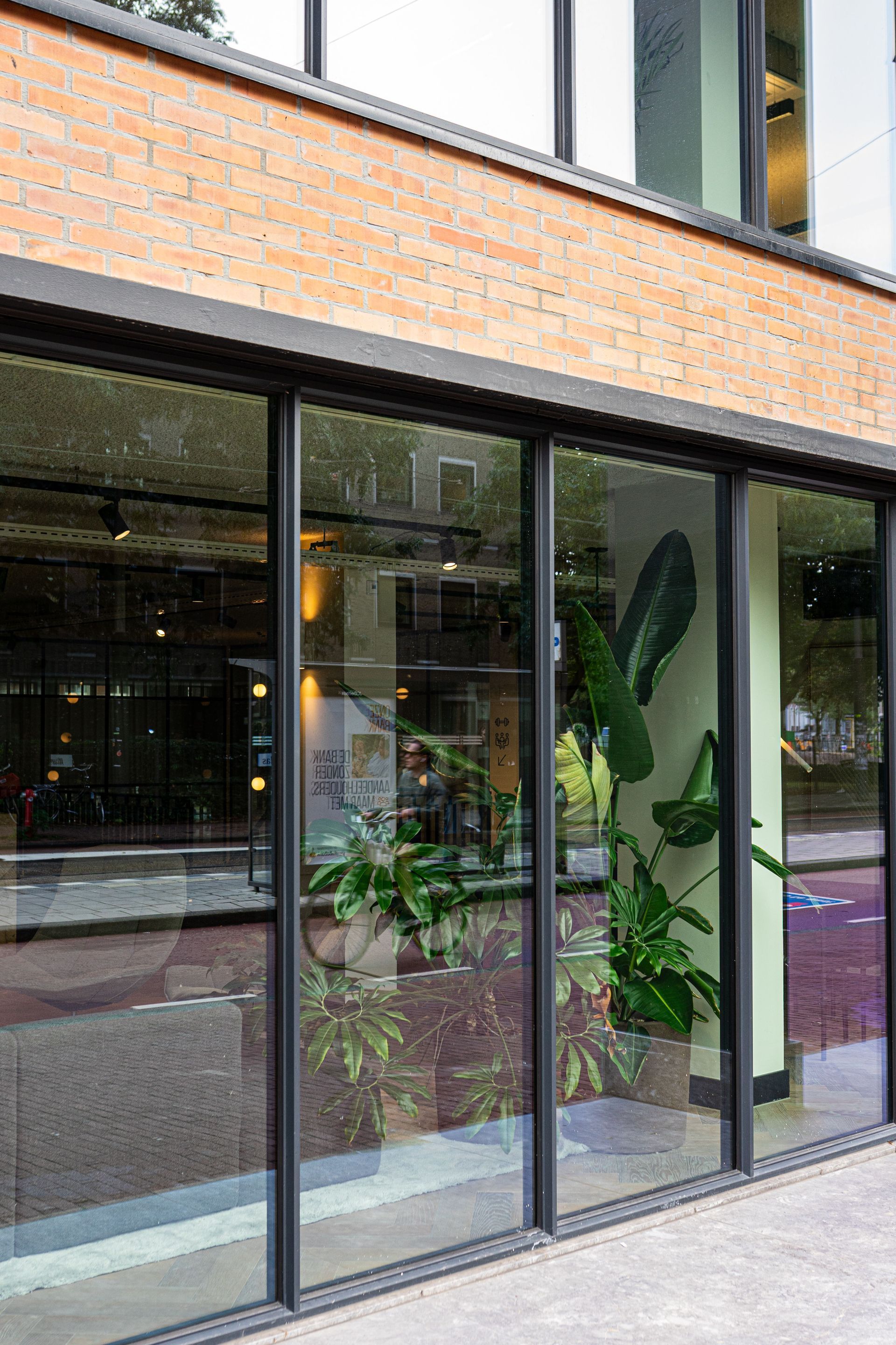 Glazen winkelpui met kamerplanten achter hoge ramen in een bakstenen gebouw