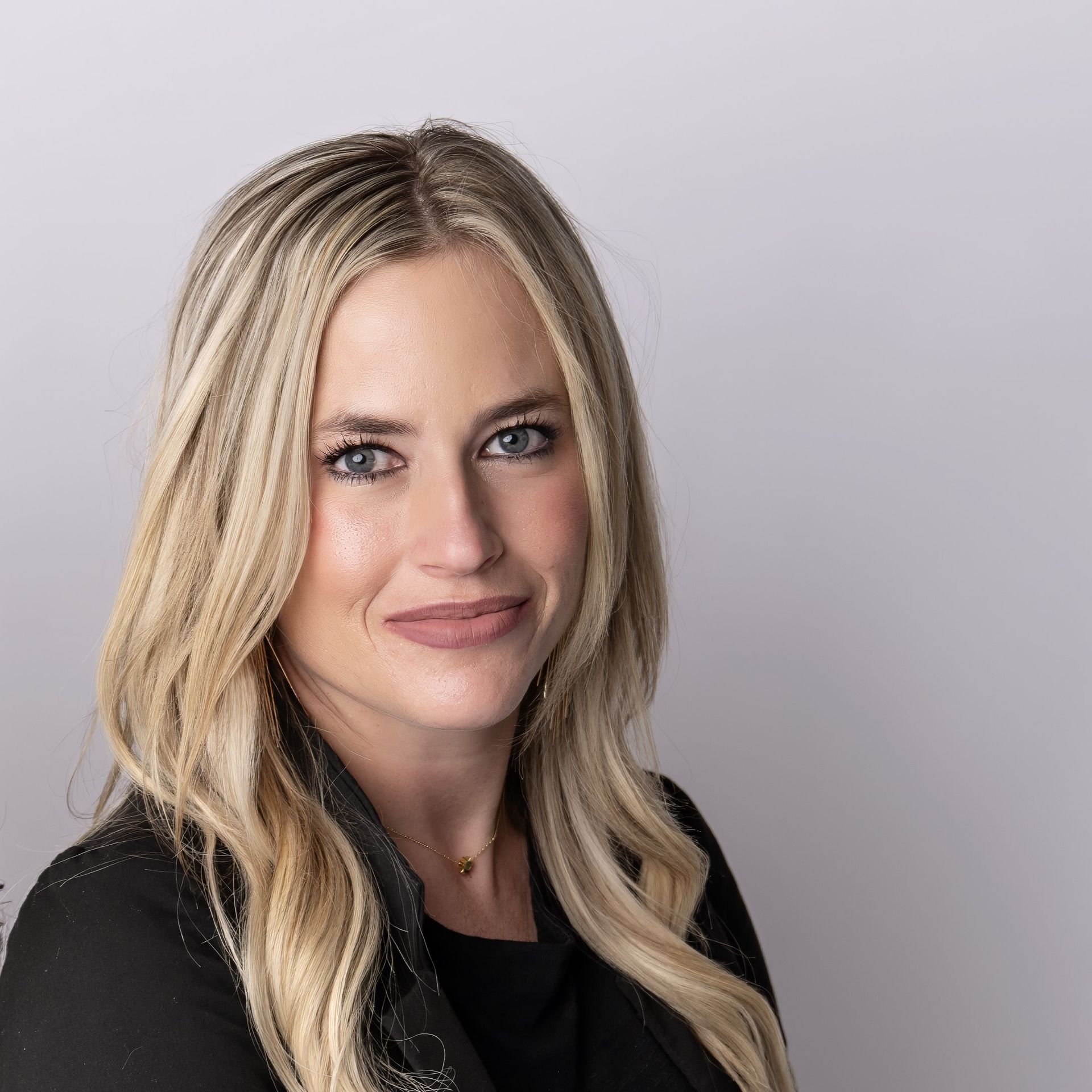 A woman with blonde hair is wearing a black shirt and smiling for the camera.