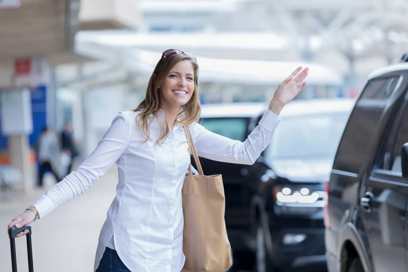 Woman with suitcase and shopping bag waving in an airport pickup area