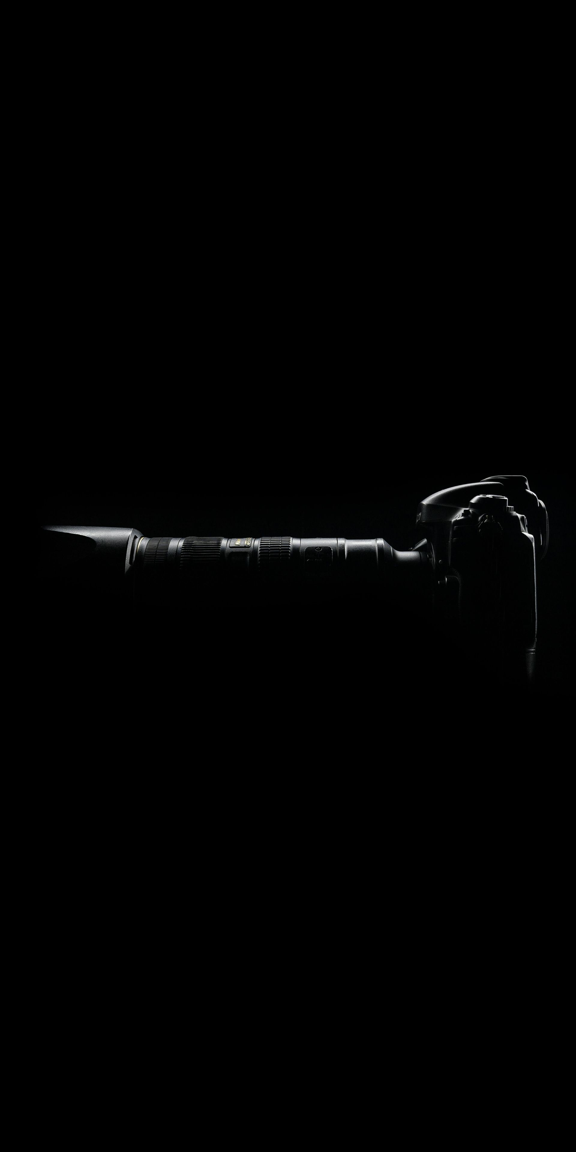 Silhouette of a camera, horizontal, with a sharp object (lens?) pointing left. Mostly dark, some highlights.