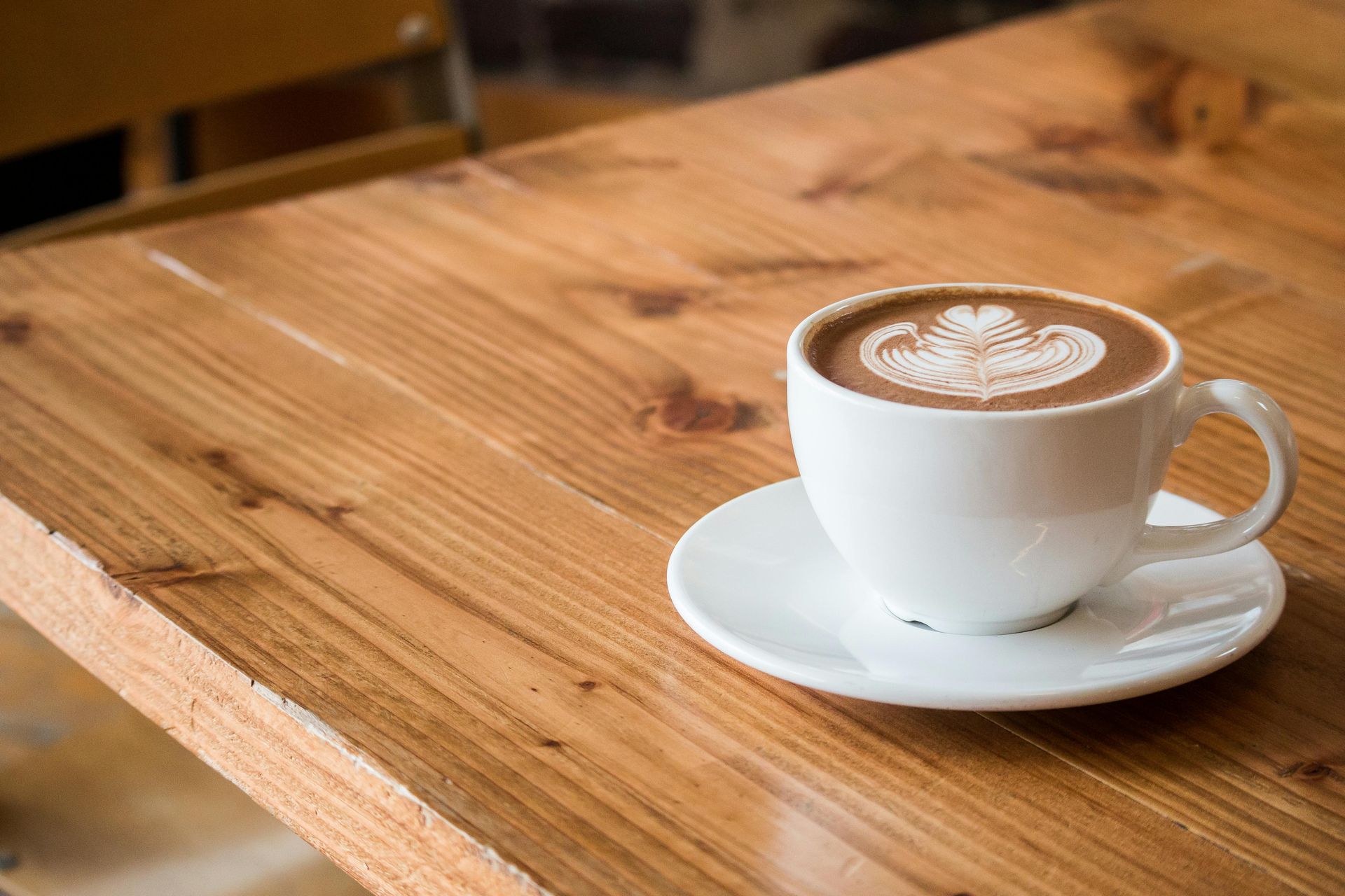 Latte in white cup with heart design on wooden table.