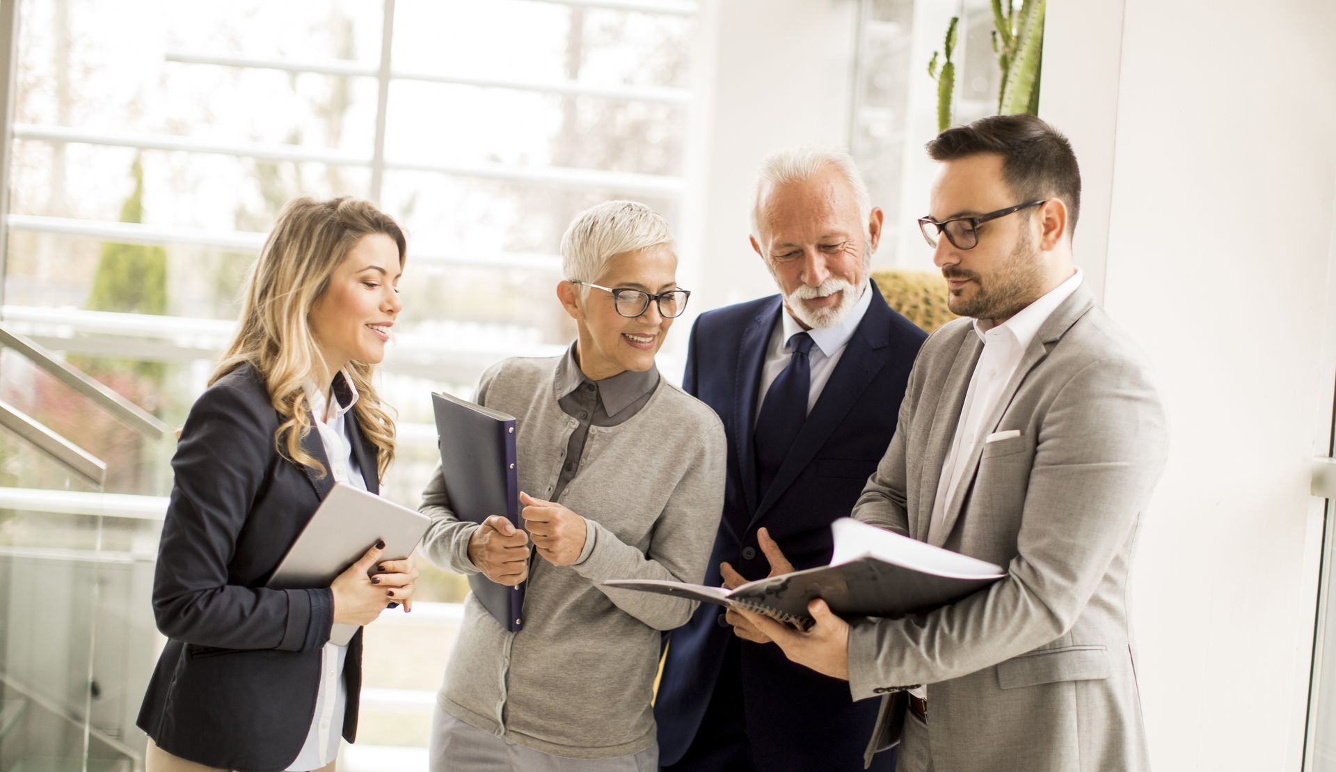 A group of business people are standing around a table looking at a clipboard.
