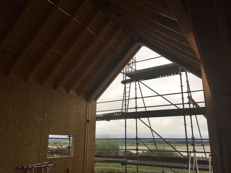 Interior of a wooden structure under construction, with scaffolding and a view of the landscape through the open frame