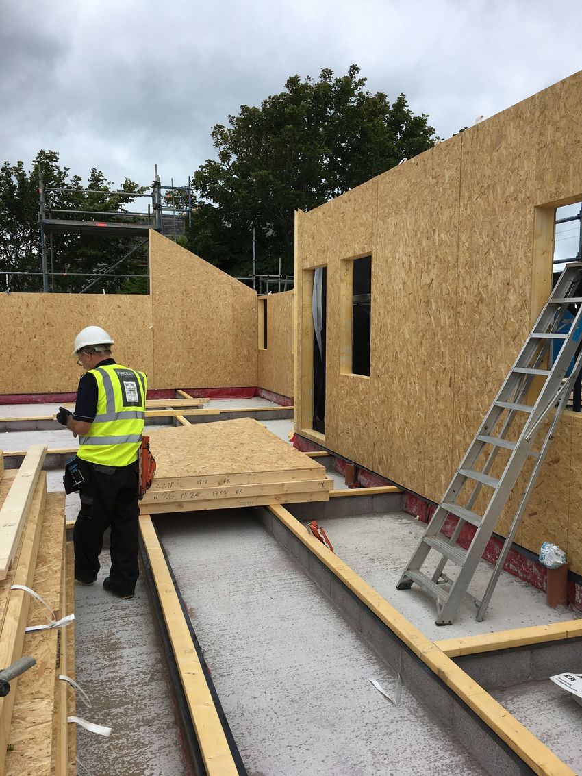 Construction site with a worker in a hi-vis vest near a partially built wooden house and ladder