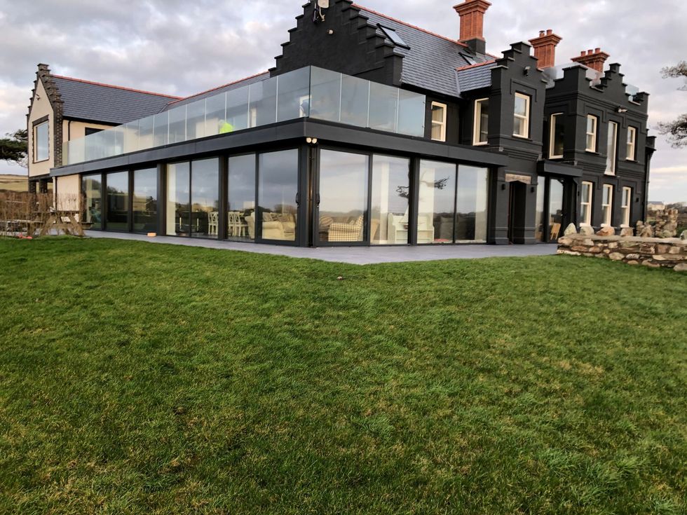 Modern black house with large glass walls and a grassy front lawn
