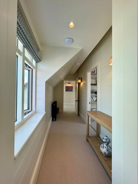 Bright hallway with windows, beige carpet, skylights, and a narrow wooden table.