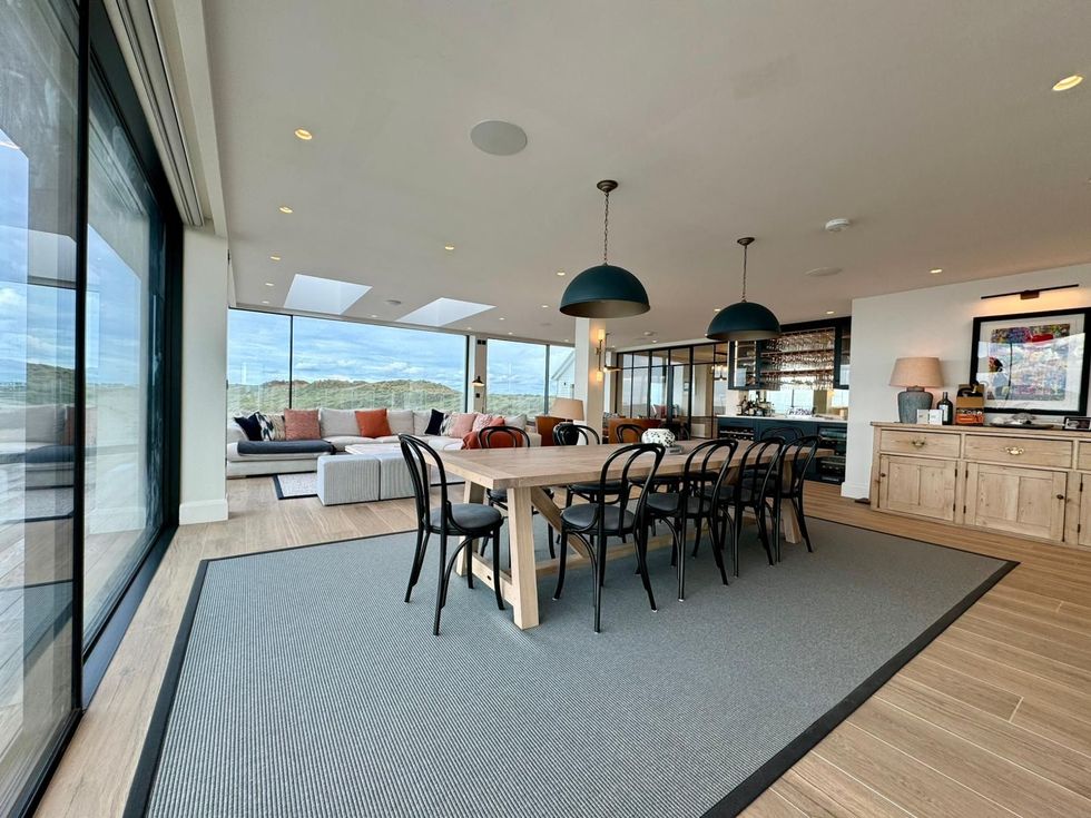 Bright modern dining room with long table, black chairs, large windows, and ocean view