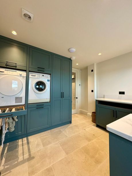 Modern laundry room with teal cabinets, stacked washer and dryer, and beige tile floor