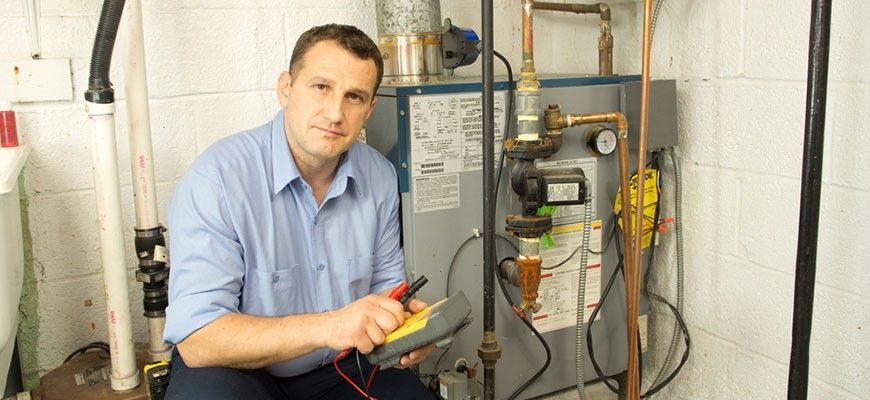 A man is sitting in a basement working on a heating system.