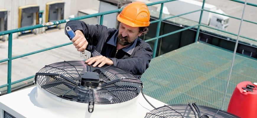 A man wearing a hard hat is working on a fan on top of a building.