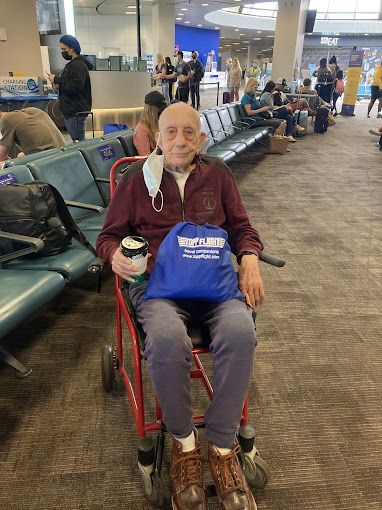 An elderly man is sitting in a wheelchair at an airport.