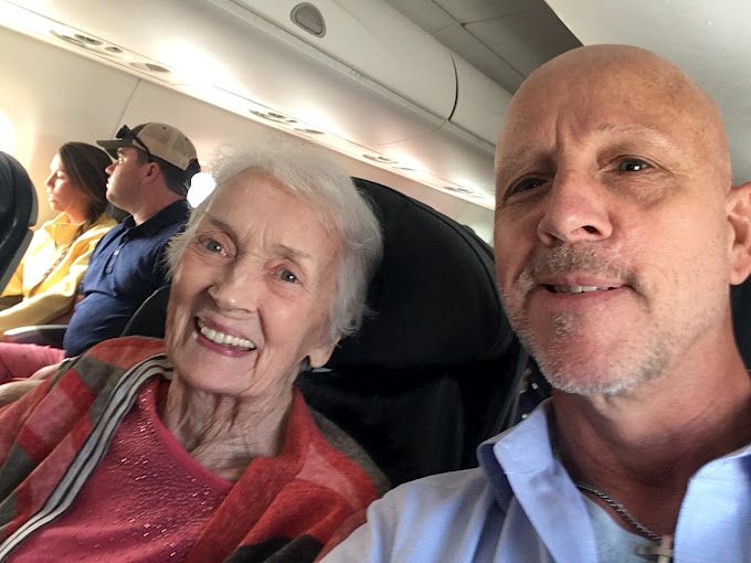 A man is taking a selfie with an elderly woman on an airplane.