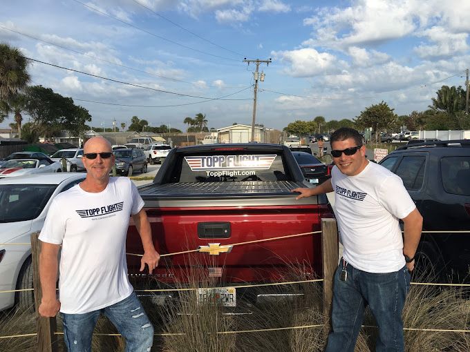 Two men in white shirts are standing next to a red truck