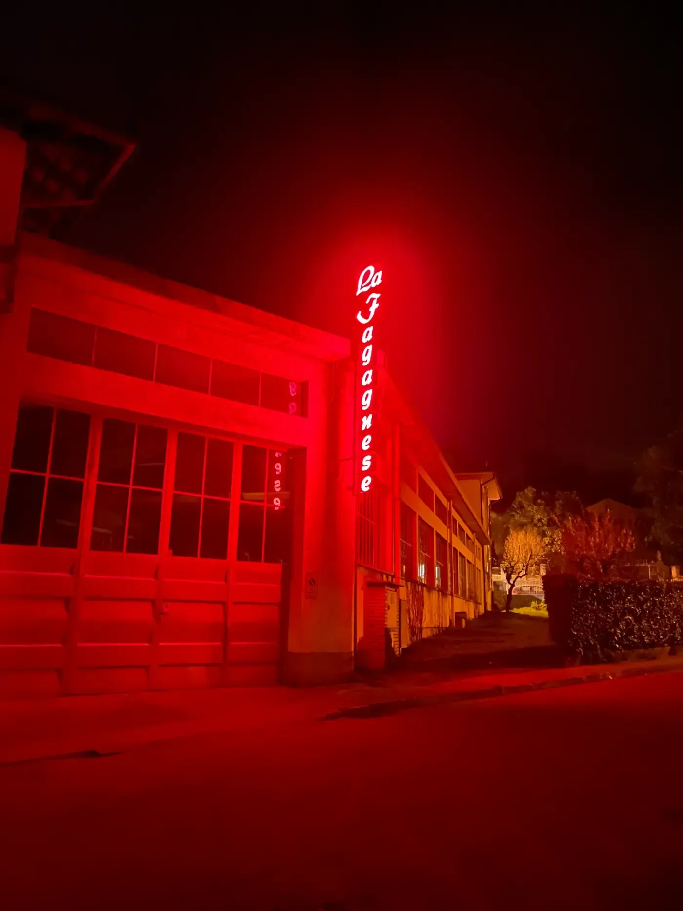 Edificio illuminato di rosso di notte con un cartello con testo bianco, probabilmente l'ingresso di un'attività commerciale.