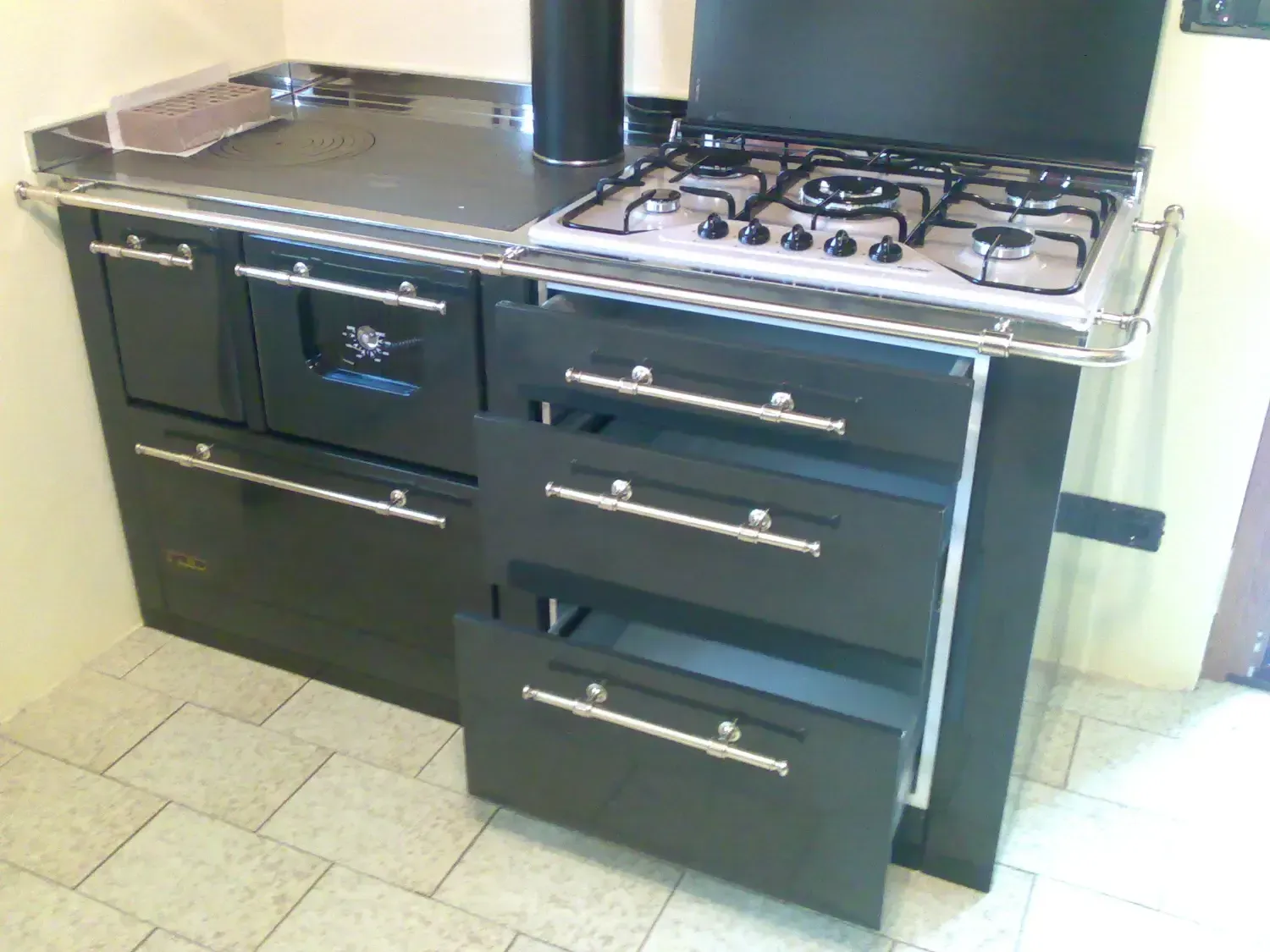 Cucina nera con piano cottura, forno e cassetti, maniglie cromate.