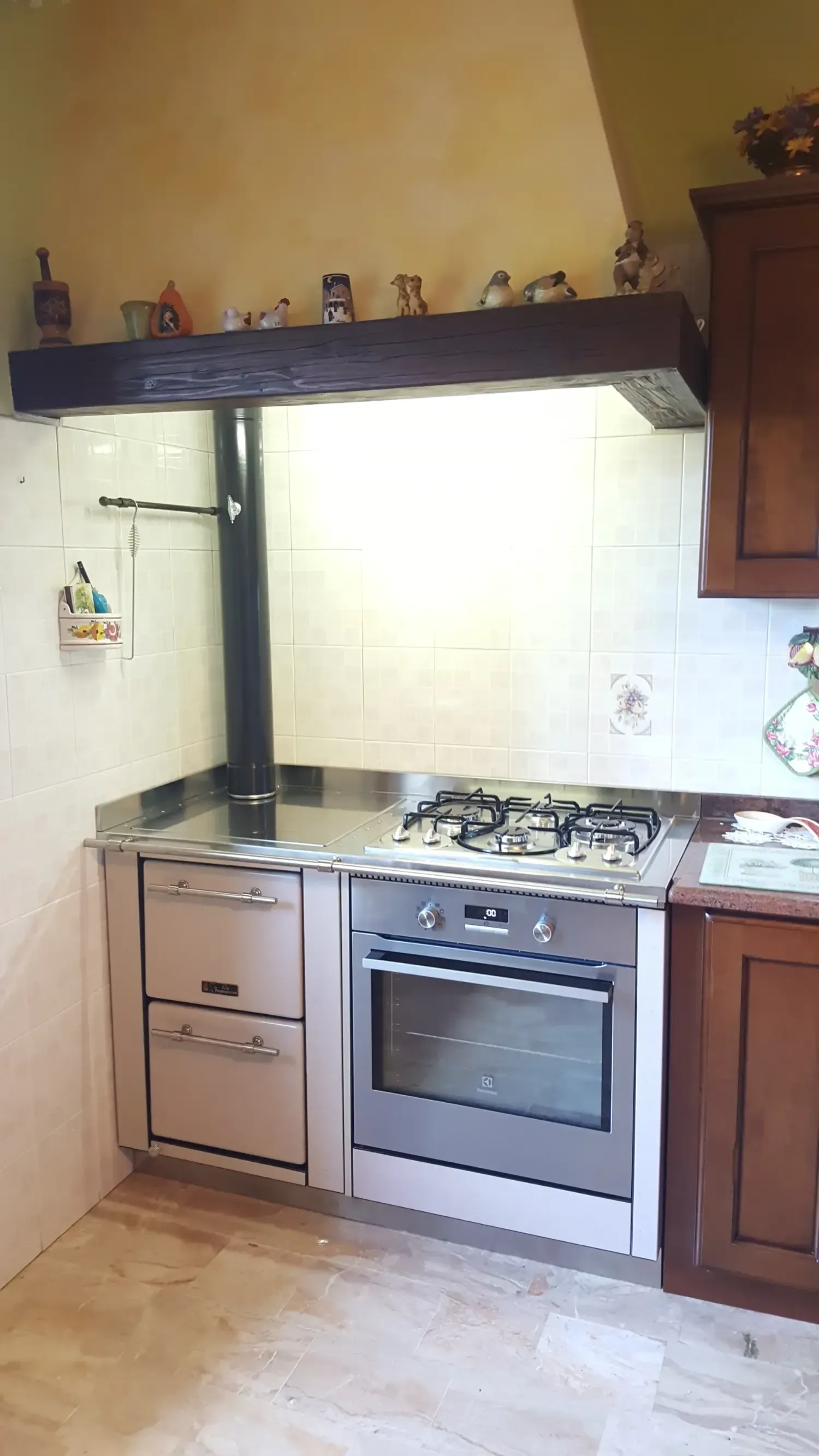 Cucina con forno e piano cottura integrati, mobili chiari, cappa scura e paraschizzi piastrellato.