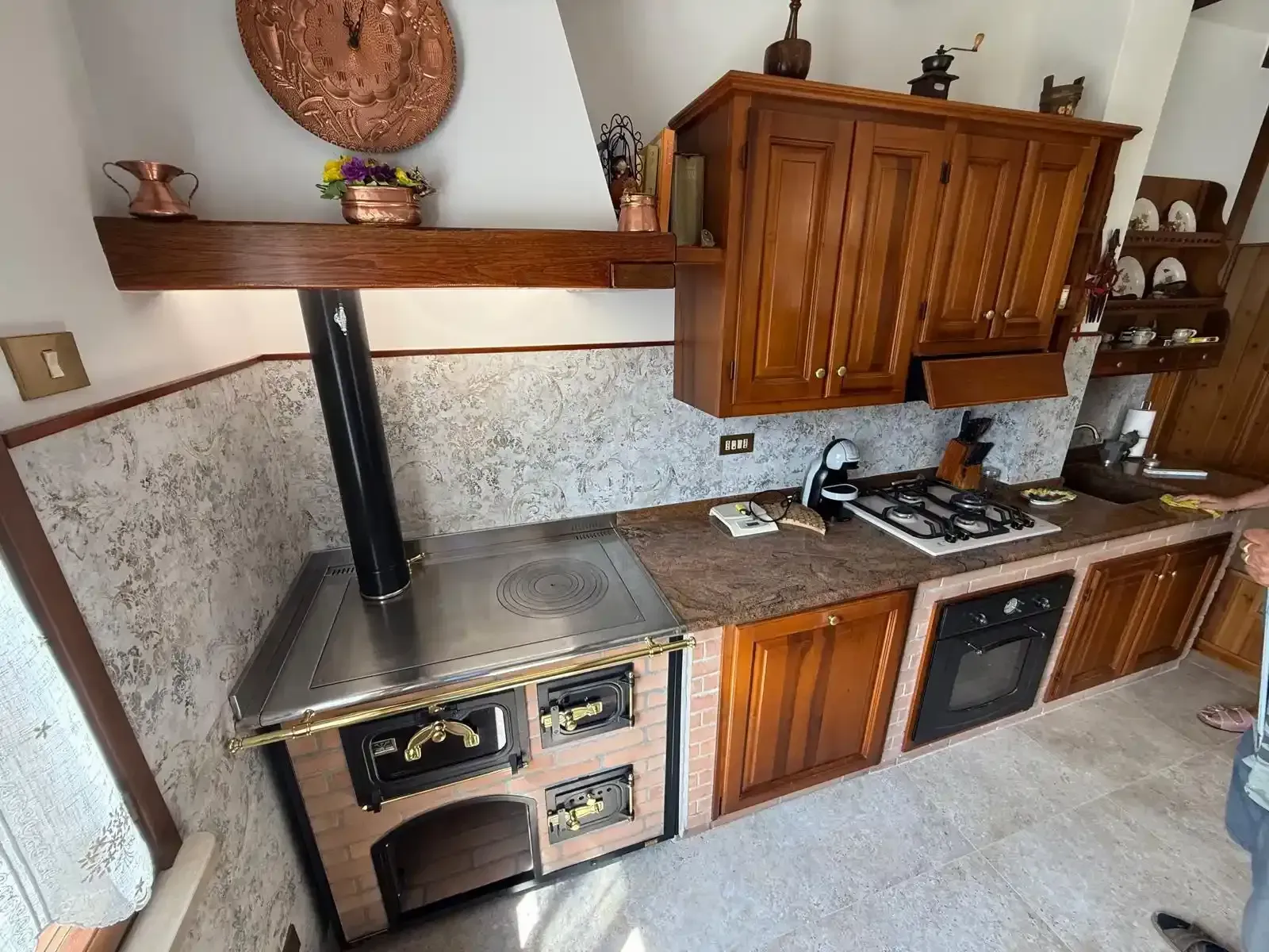 Stufa a legna con rivestimento esterno in piastrelle verdi, piano superiore in metallo e fiamme a vista. Ambiente cucina.