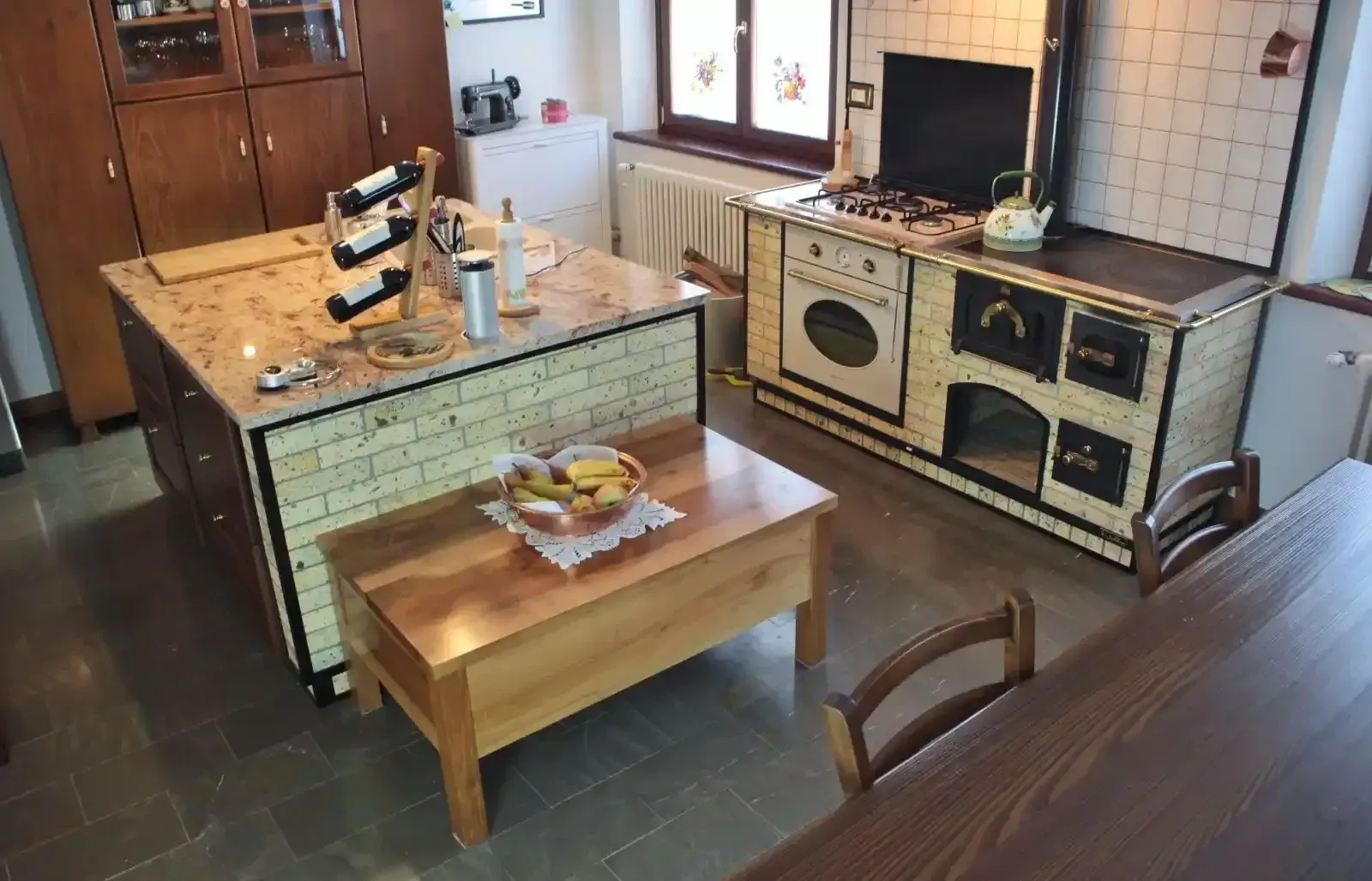Cucina rustica con stufa a legna, mobili in legno e tavolo da pranzo, illuminata in modo caldo.