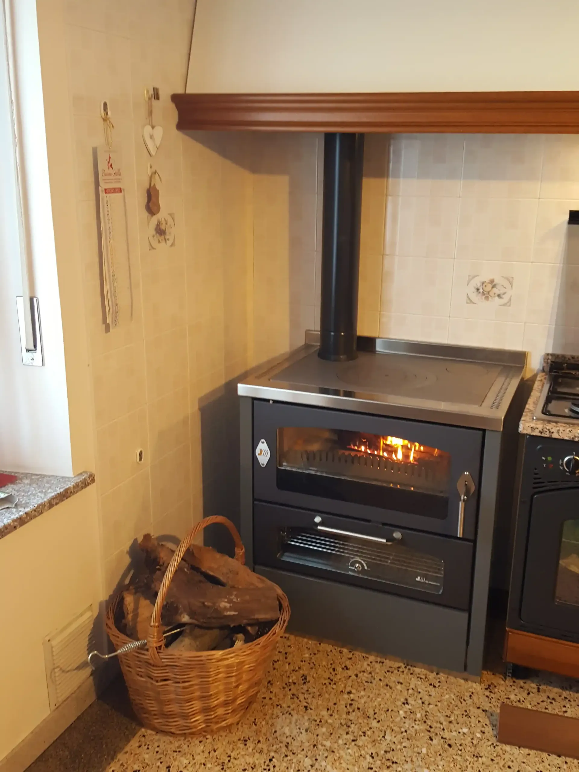 Stufa a legna con fuoco acceso, camino in metallo e cestello per la legna in una cucina.