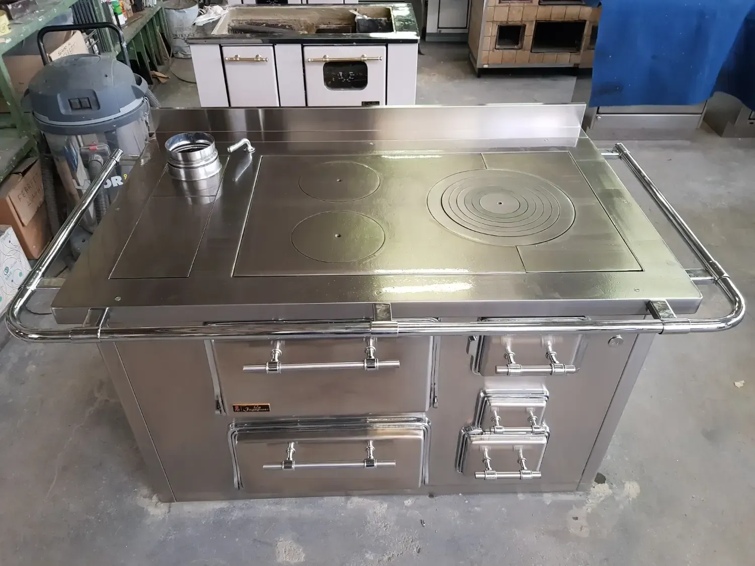 Stufa a legna in acciaio inox con piano cottura, cassetti e forno. Una seconda stufa è sullo sfondo.