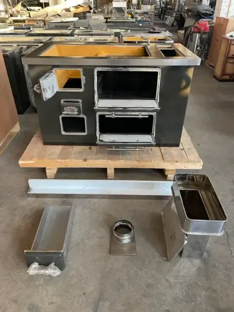 Fornello da cucina in metallo nero su pallet di legno con componenti separati. Ambiente da officina.