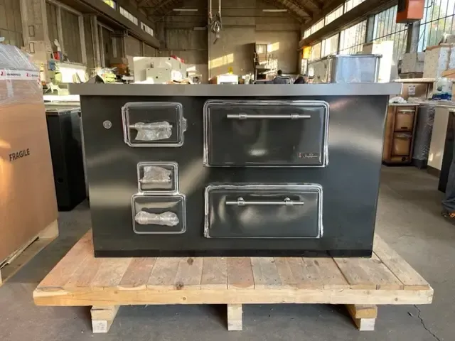 Cucina industriale grigio scuro con sportelli del forno trasparenti su pallet di legno.