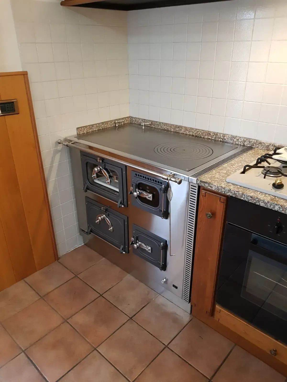 Cucina in acciaio inox con due forni, piano cottura e piano cottura. Cucina angolare, pareti e pavimento piastrellati.