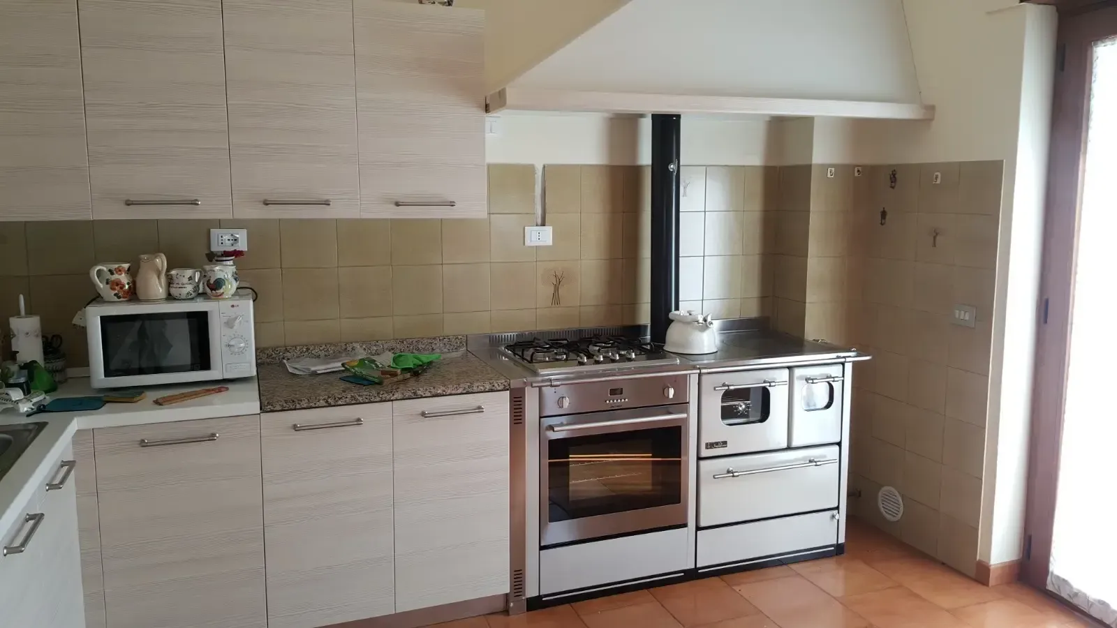 Cucina con piano cottura in acciaio inox, forno e focolare a legna. Design rustico con mobili in legno.