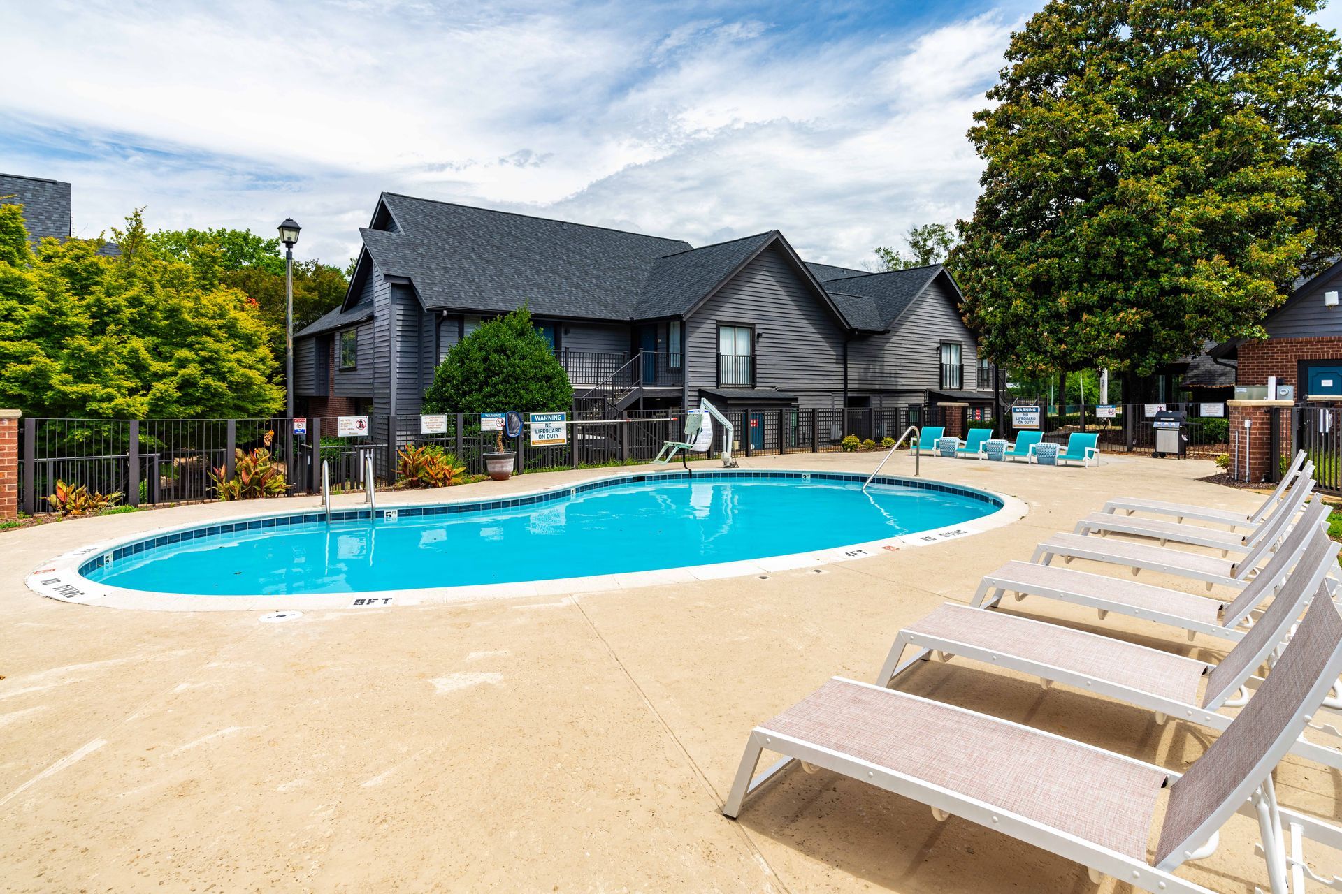 Outdoor pool with lounge chairs beside a gray resort building under a blue sky