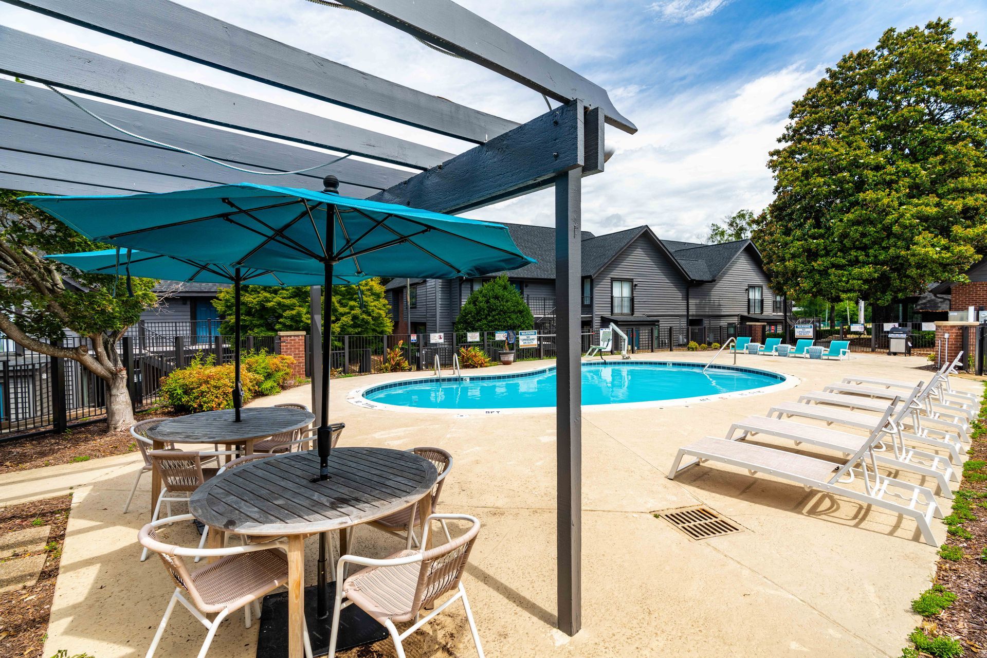Outdoor pool with lounge chairs and shaded patio tables at a resort