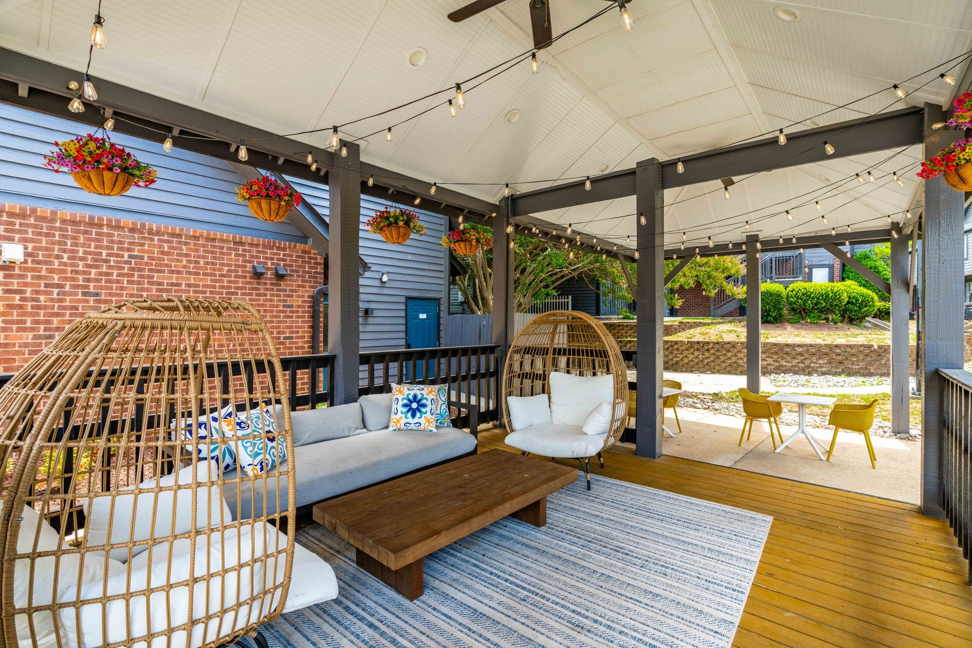 Covered patio with wicker chairs, a low table, hanging flowers, and a striped rug