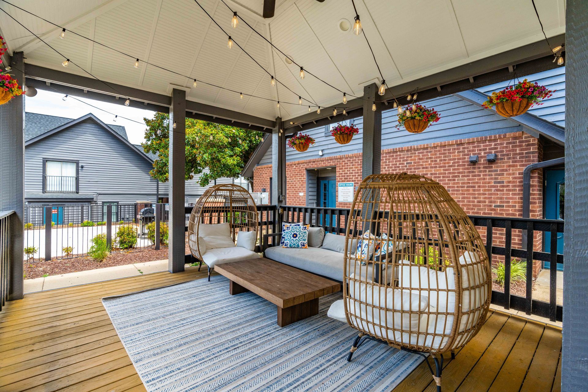 Covered porch with wicker swing chairs, rug, and wooden table in front of a brick house.