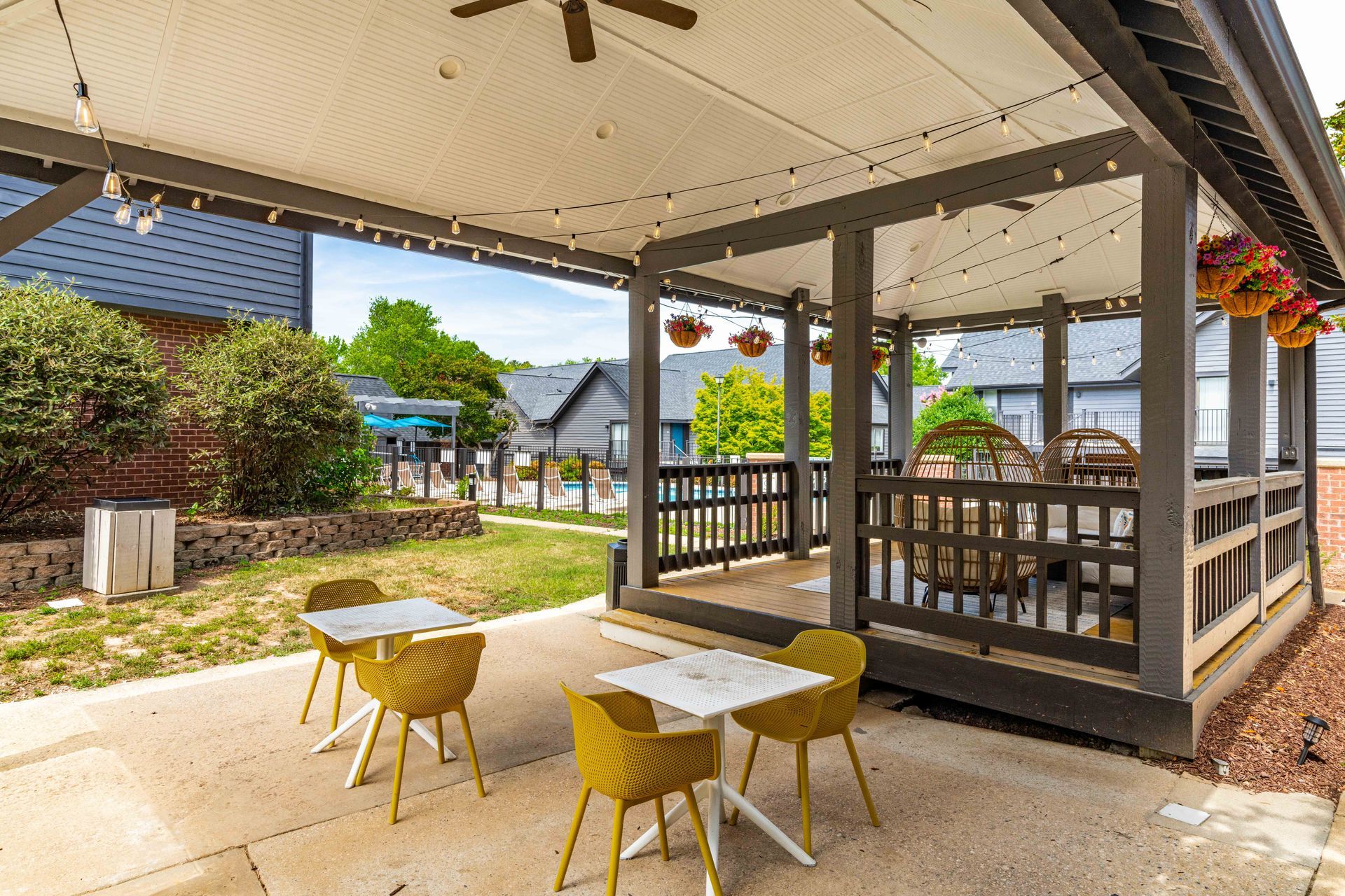 Covered patio seating with yellow chairs and tables beside a residential yard and walkway