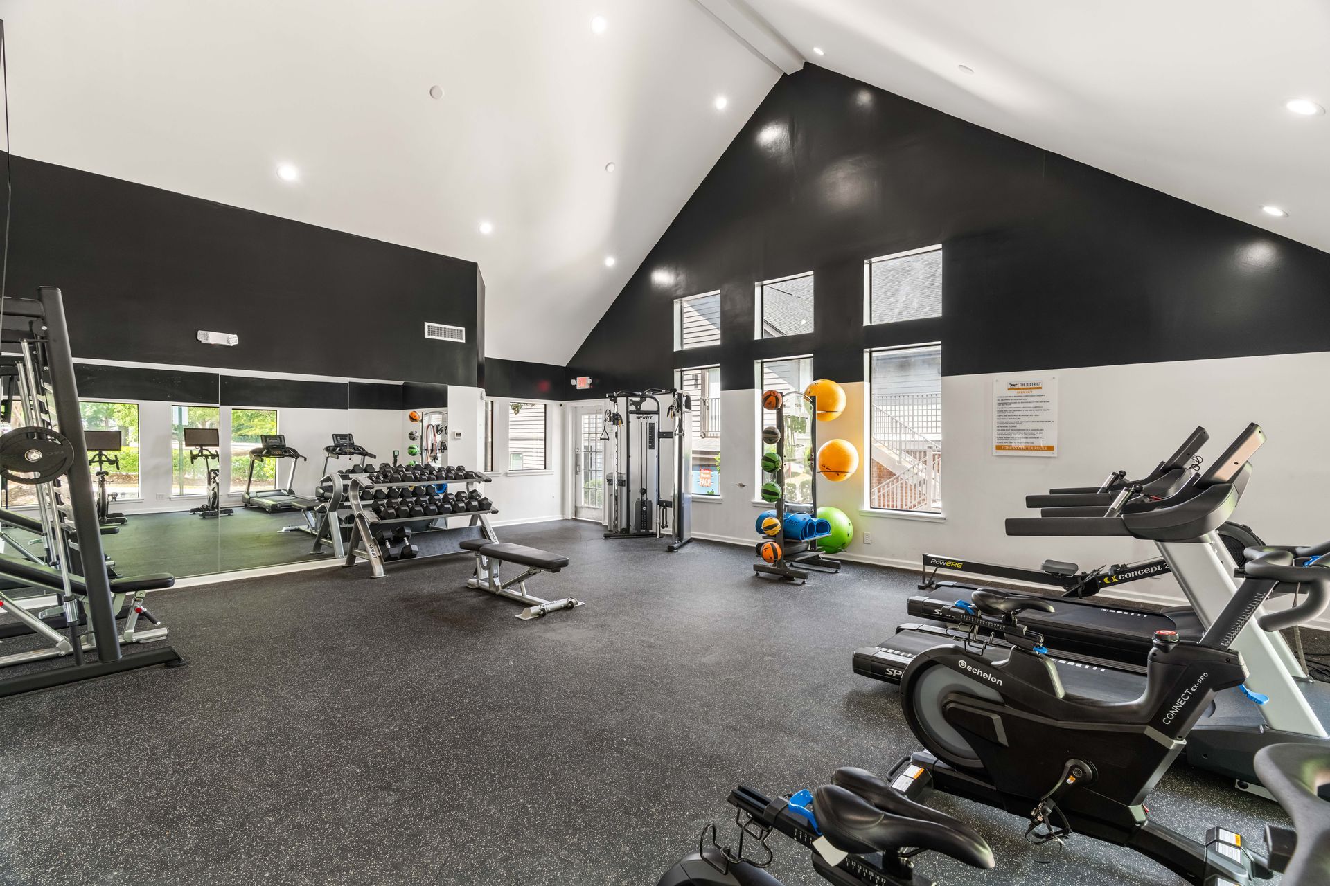 Modern gym interior with treadmills, weight bench, and exercise machines on black rubber flooring.