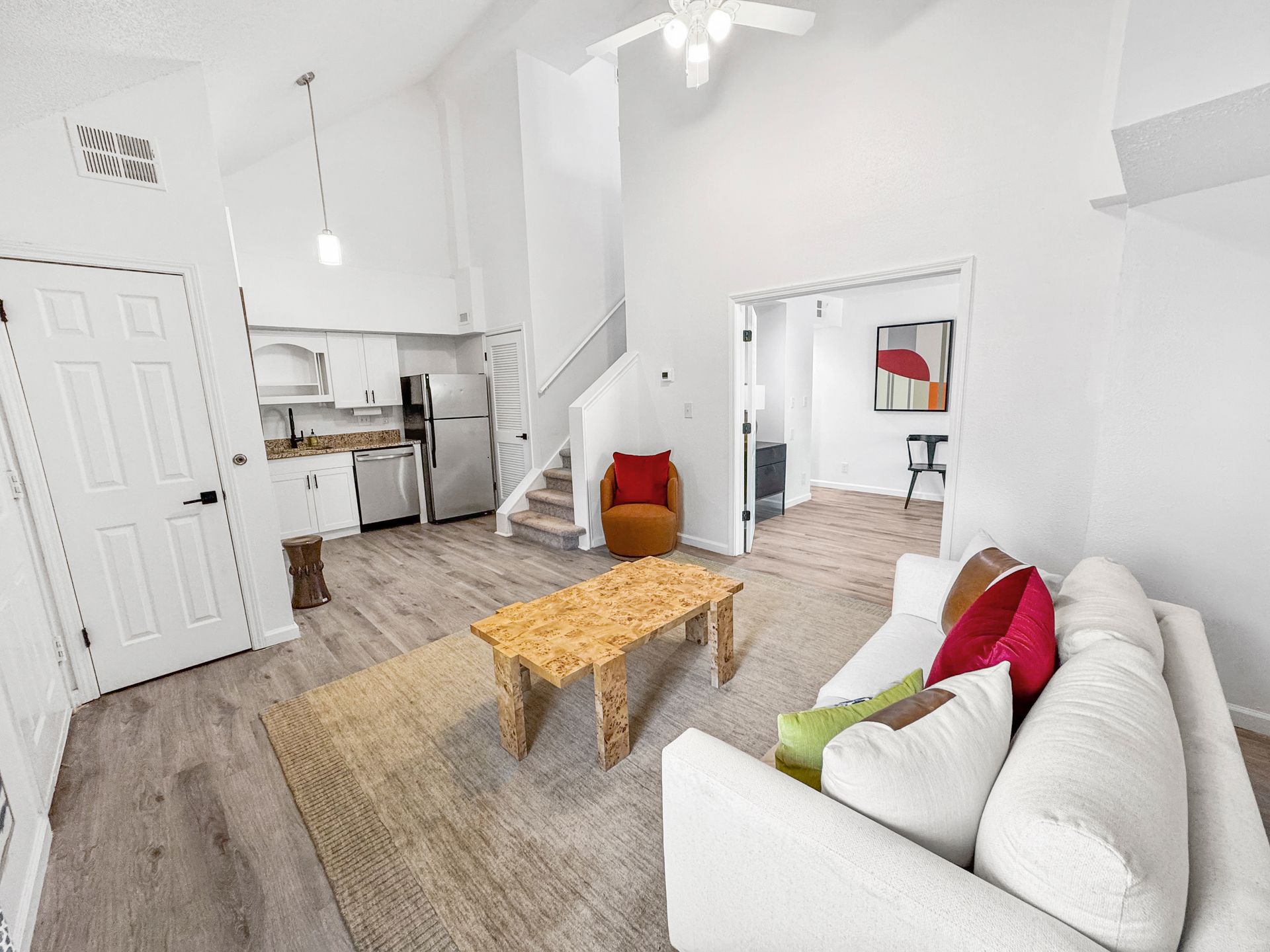 Bright white open-plan living room with sofa, coffee table, stairs, and kitchen area