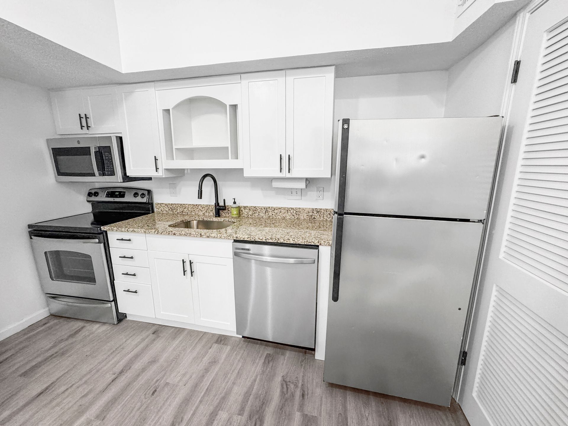 Compact kitchen with stainless steel appliances, white cabinets, granite countertop, and wood-look flooring