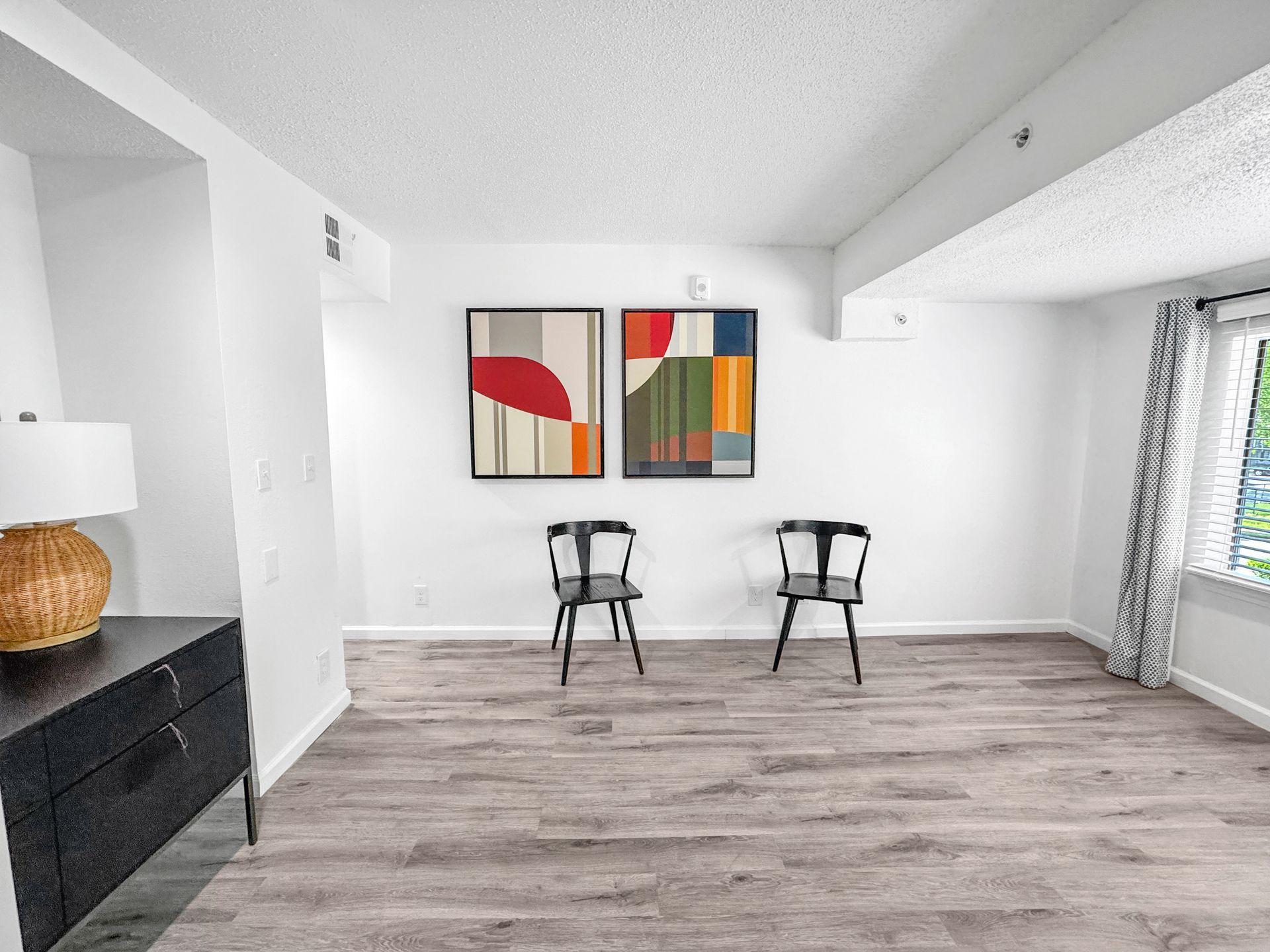 Bright minimalist room with two chairs, abstract wall art, and wood-look flooring