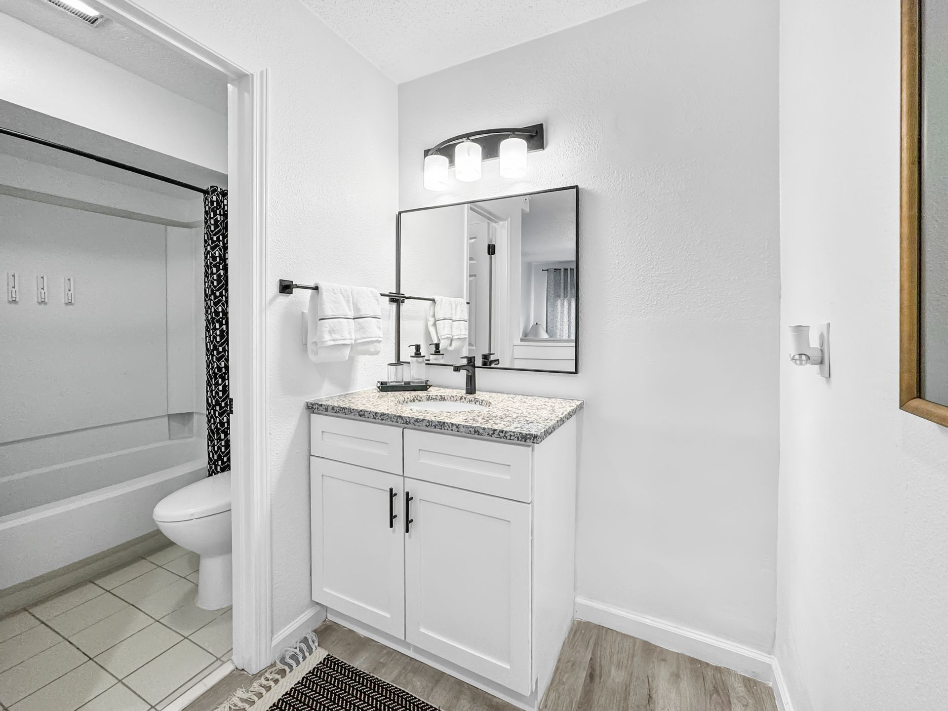 Small bathroom vanity with white cabinets, granite countertop, mirror, and a bathtub visible through the doorway