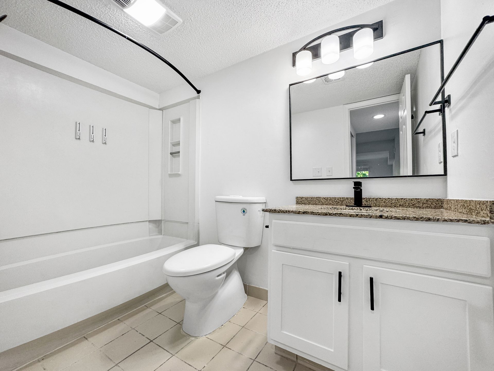 Bright white bathroom with tub, toilet, vanity sink, mirror, and granite countertop.