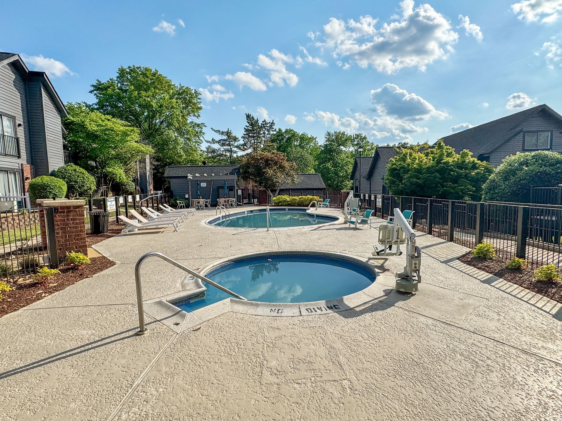 Outdoor pool and hot tub in a sunny courtyard with lounge chairs and greenery
