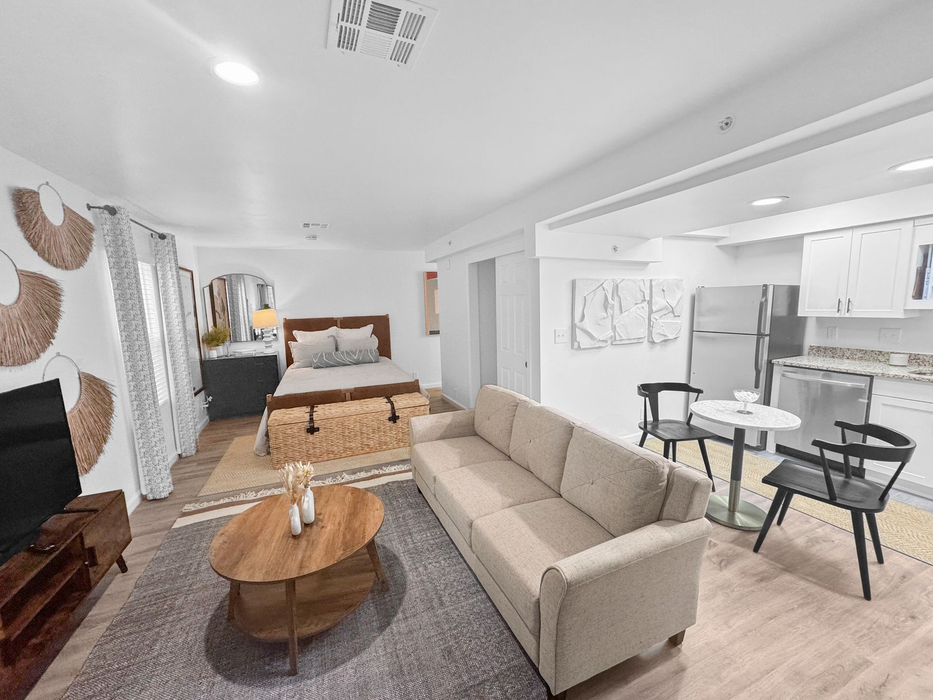Bright living room with beige sofa, round coffee table, fireplace, and small dining area opening to a bedroom.