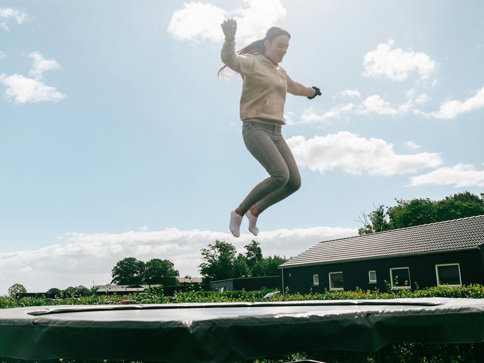 Young woman jumping high on an outdoor trampoline in a backyard