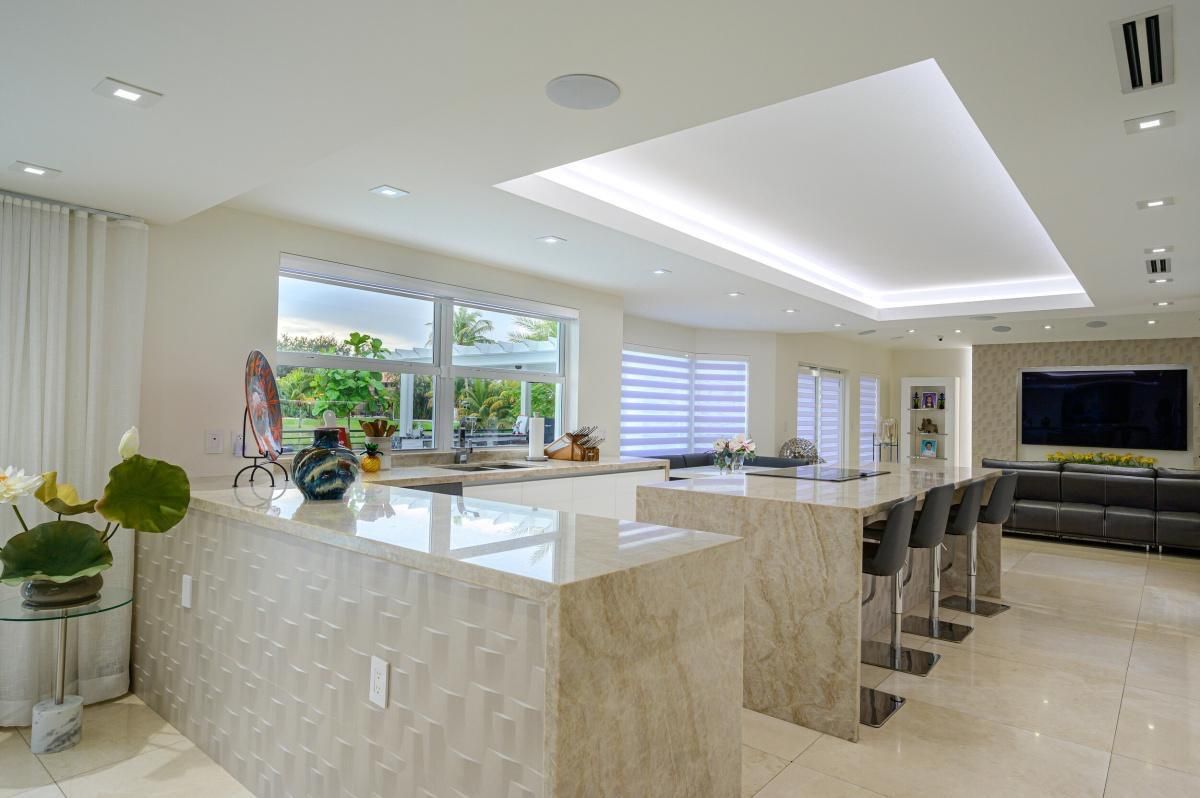 Bright modern kitchen with marble island, bar stools, and large windows overlooking greenery