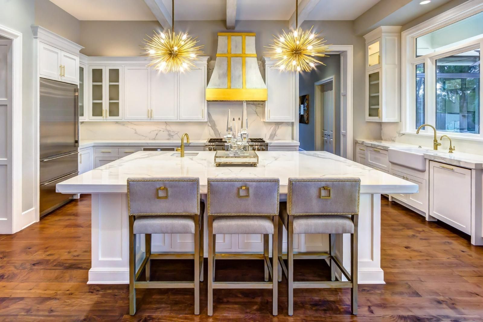 Bright modern kitchen with a large island, three stools, pendant lights, and hardwood floors.