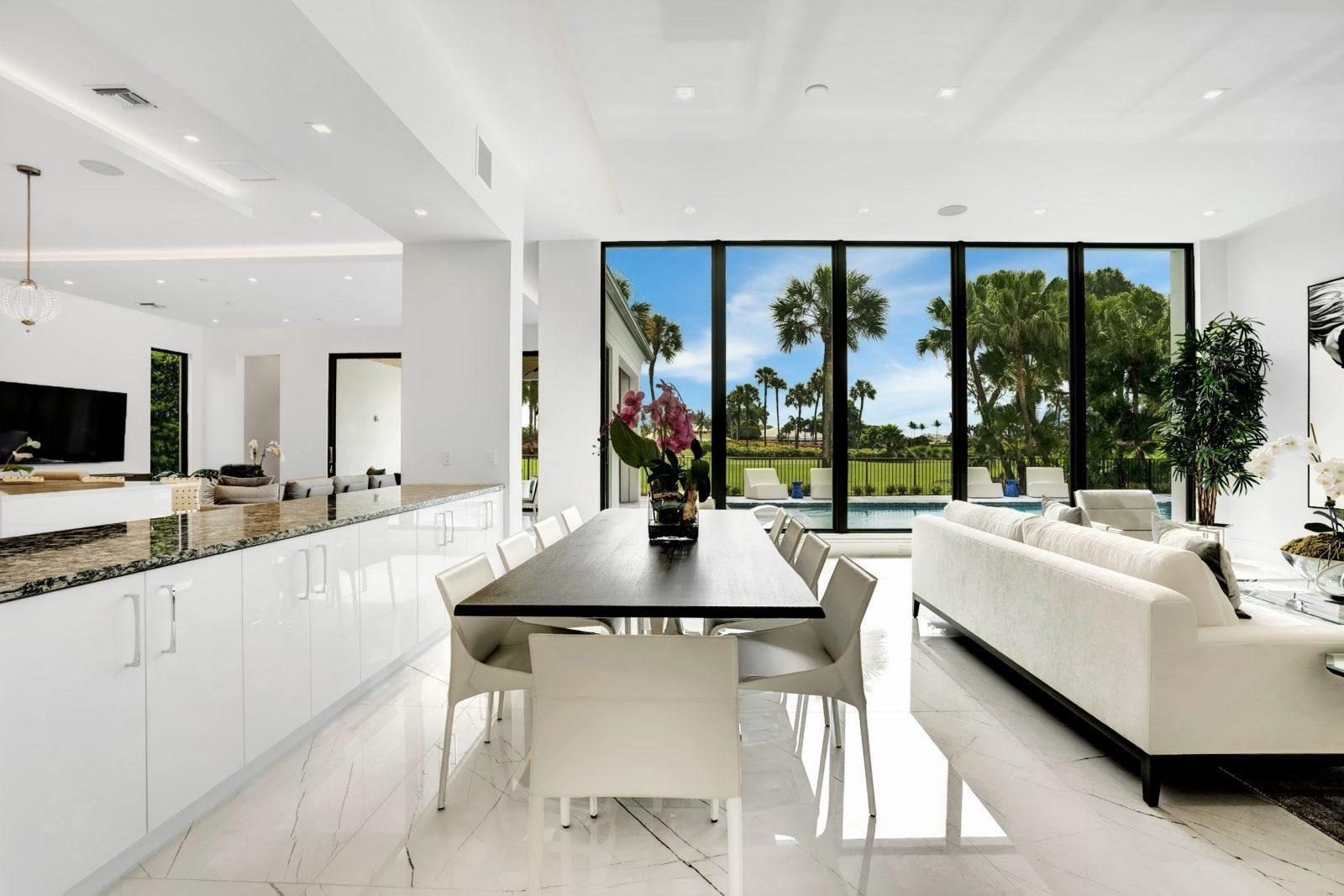Bright modern open-plan living room with white furnishings, kitchen island, and large glass doors to a sunny patio