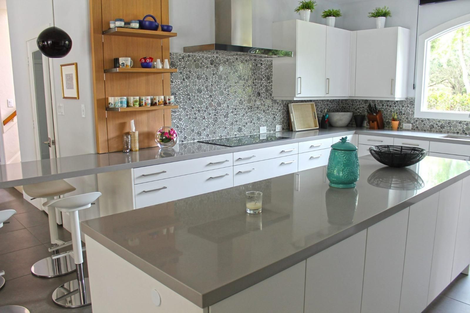 Modern kitchen with white cabinets, gray island, mosaic backsplash, and stools by the counter.
